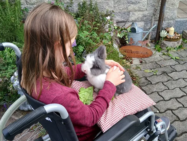 Kind von Hinten im Rollstuhl fotografiert, sie streichelt einen Hasen.